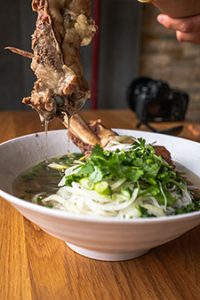 Bowl of pho topped with rib bones, herbs, onions, and scallions